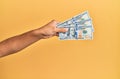 Hand of hispanic man holding 100 dollars banknotes over isolated yellow background Royalty Free Stock Photo