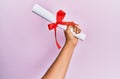 Hand of hispanic man holding graduated diploma over pink background