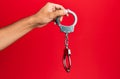 Hand of hispanic man holding handcuffs over isolated red background Royalty Free Stock Photo