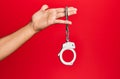 Hand of hispanic man holding handcuffs over  red background Royalty Free Stock Photo