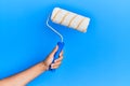 Hand of hispanic man holding paint roller over isolated blue background Royalty Free Stock Photo