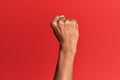 Hand of hispanic man over red isolated background doing protest and revolution gesture, fist expressing force and power