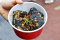 A Hand Hoiding A Box with Black Deep Fried Stinky Tofu.