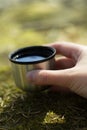 Hand hold cup of hot tee or coffe on mossy rock