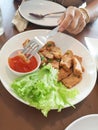 Hand hold fork stabbing fried pork chop on white dish with chilli sauce.