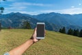 Hand hold mobile phone in mountains and field landscape and the blue sky with clouds Royalty Free Stock Photo