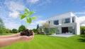 Hand hold seedling with modern, energy-efficient home in background, embracing eco-design, reducing SO2 emissions