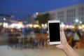 hand hold and touch screen smart phone, on blurred photo of people shopping at night market. Royalty Free Stock Photo