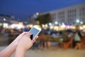 hand hold and touch screen smart phone, on blurred photo of people shopping at night market. Royalty Free Stock Photo