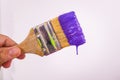 Hand holdig a paintbrush angled purple wet paint dripping from brush