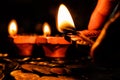Hand holdin an earthen lamp to light other lamps on a pile of coins for Diwali decoration. Prosperity and hope concept