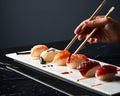 Hand holding bamboo chopsticks with nigiri. Detail of sushi at restaurant. Front view. Food, Japanese cuisine concept Royalty Free Stock Photo