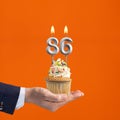 Hand holding birthday cupcake with number 86 candle - background orange
