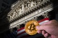 Hand holding a bitcoin and blurred NYSE in the background