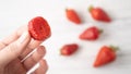 Hand holding bitten strawberry on white wooden background. Summer berry pleasure. Scattered strawberries