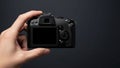 A hand is holding a black digital camera, viewed from the back Royalty Free Stock Photo