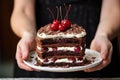 hand holding a black forest cake topped with cream and cherries Royalty Free Stock Photo