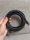 hand holding black lan cable with plug on gray fabric background