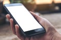 A hand holding black mobile phone with blank white desktop screen on vintage wooden table in cafe Royalty Free Stock Photo