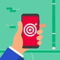 Hand holding black mobile phone with target aim with arrow in bullseye symbol icon sign on the screen isolated on wall background. Royalty Free Stock Photo