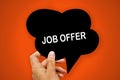 Hand holding black paper speech bubble with JOB OFFER concept, over orange background, .