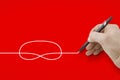 Hand holding a black pencil drawing a knot on red background Royalty Free Stock Photo