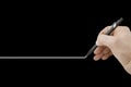 Hand holding a black pencil drawing a perfectly straight white line on black background Royalty Free Stock Photo
