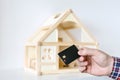 Hand holding black plastic chip keycard. Wooden house model on background. Security lock. Wireless entrance unlock key Royalty Free Stock Photo