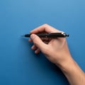 A hand holding a black and silver pen is poised above a solid blue Royalty Free Stock Photo