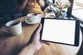 A hand holding black tablet pc with white blank screen on wooden table with woman using mobile phone in backgroun Royalty Free Stock Photo