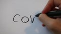 Hand holding black thick permanent marker and writing the word covid