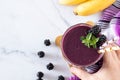 Hand-holding blackberry banana smoothie with fresh mint in a glass with eco-friendly straws on white marble table, top view Royalty Free Stock Photo