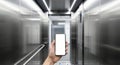 A hand holding a blank smartphone inside a sleek, metallic elevator with open doors and bright lighting, emphasizing Royalty Free Stock Photo