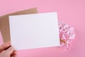 Hand holding blank wedding invitation stationery card mockup with envelope on pink background with hyacinth flowers, Royalty Free Stock Photo