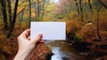 hand holding blank white card against orange autumn rainforest background