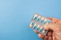 Hand holding blister pack of blue and white pills on blue backgr Royalty Free Stock Photo