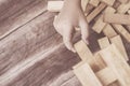 Hand holding blocks wood game (jenga) on wooden plank background Royalty Free Stock Photo