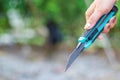 Hand holding blue cutter Knife on green natural blur background.