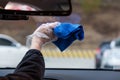 Hand holding a blue fiber towel to wipe the car window. Cleaning car`s windshield with microfiber cloth