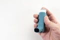 Hand holding a blue inhaler, also known as pump or allergy spray, medical device for asthma or COPD patients, light background, Royalty Free Stock Photo