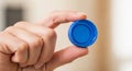 A hand is holding a blue plastic bottle cap between the thumb and index finger. The c Royalty Free Stock Photo