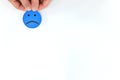 Hand holding a blue sad emoticon in white background with copy space. Unsatisfied client and bad customer service concept.