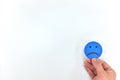 Hand holding a blue sad face in white background with copy space. Negative customer feedback and review, bad service concept.