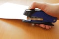 Hand holding blue stapler stapling papers