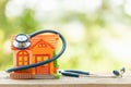 Hand holding blue stethoscope and orange house model on wooden table. Home and building checking Royalty Free Stock Photo