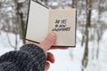 Hand holding a book with the inscription Say yes to new adventures on the background of the winter forest Royalty Free Stock Photo