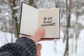Hand holding a book with the inscription Say yes to new adventures on the background of the winter forest Royalty Free Stock Photo