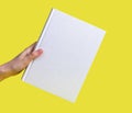 Hand holding book mockup on yellow background. Education, reading leisure, wisdom, intellectual development concept.