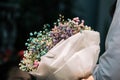 Hand holding bouquet of dried gypsophila flowers wrapped in paper