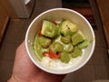 Hand holding bowl of cheesy pasta with avocado